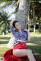 A woman in a red skirt leaning against a tree.