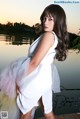 A woman in a white dress posing by a lake.