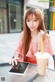 A woman sitting at a table with a tablet and a drink.