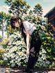 A girl with a backpack standing in front of a bush of flowers.