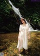 A woman in a white dress standing in front of a waterfall.